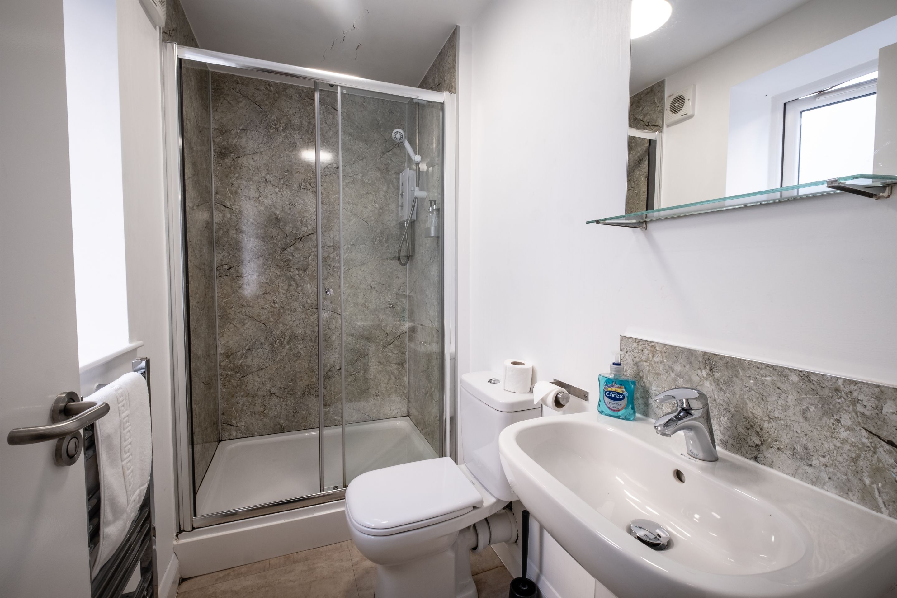 Un baño con ducha, inodoro, lavabo y un estante de vidrio.