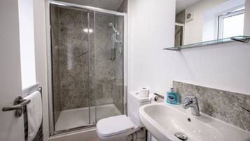 Un baño con ducha, inodoro, lavabo y un estante de vidrio.