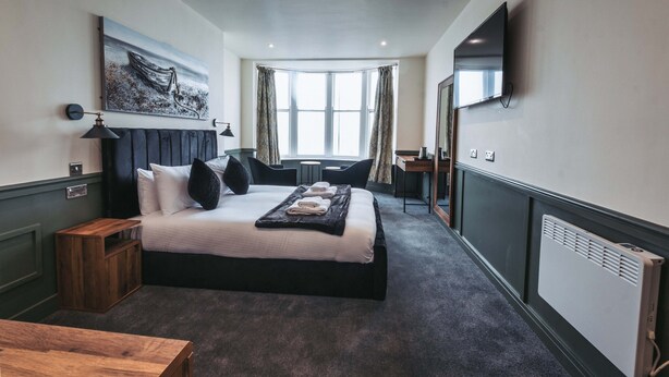 Una habitación de hotel con cama, escritorio, silla, televisor, un cuadro y ventana.