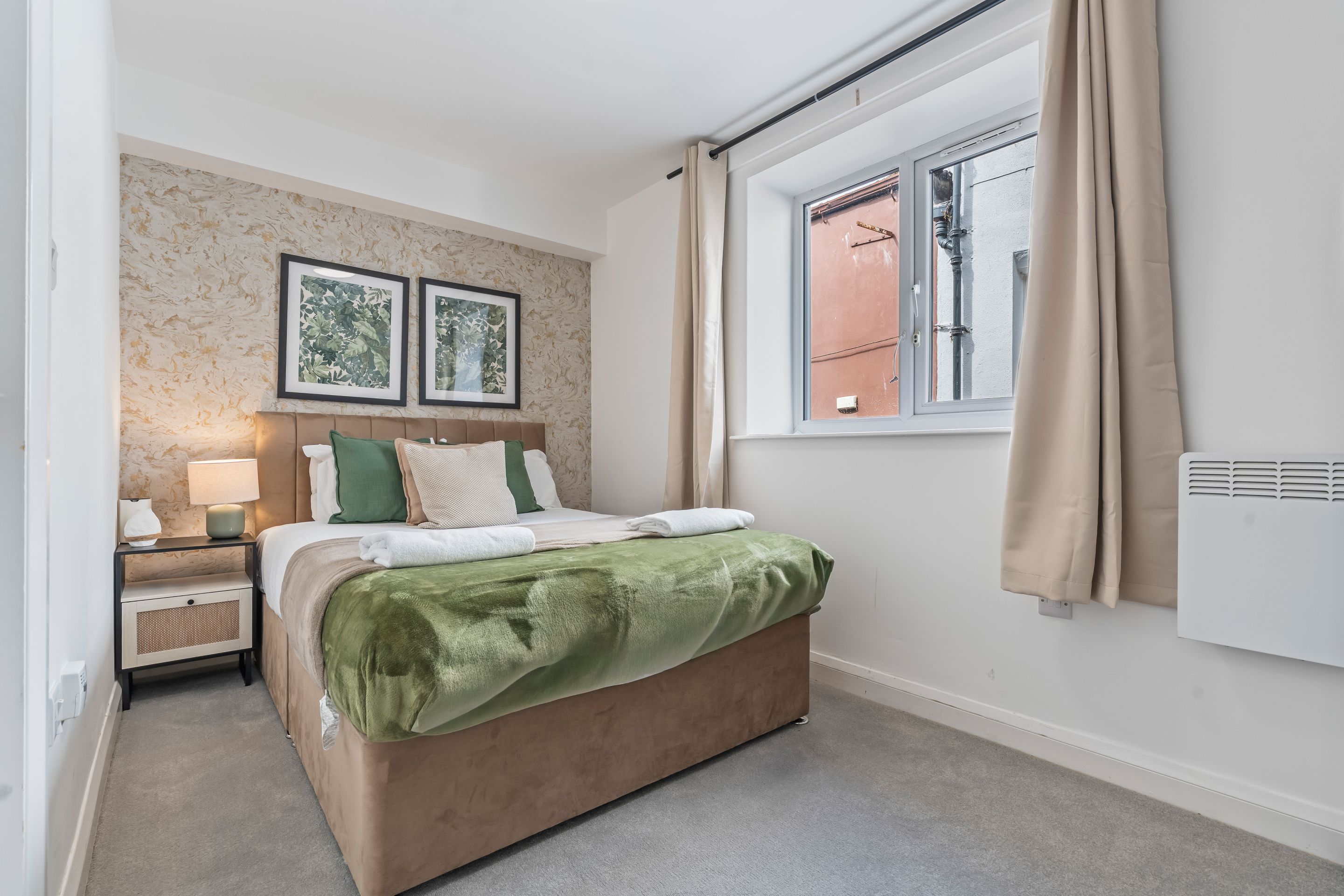 A bedroom with a bed, nightstand, lamp, and two framed pictures on the wall.