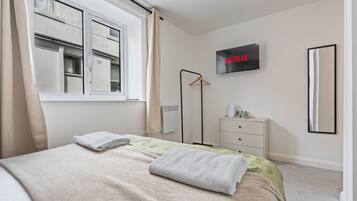 Un dormitorio con cama, televisión en la pared, cómoda y ventana con cortinas.