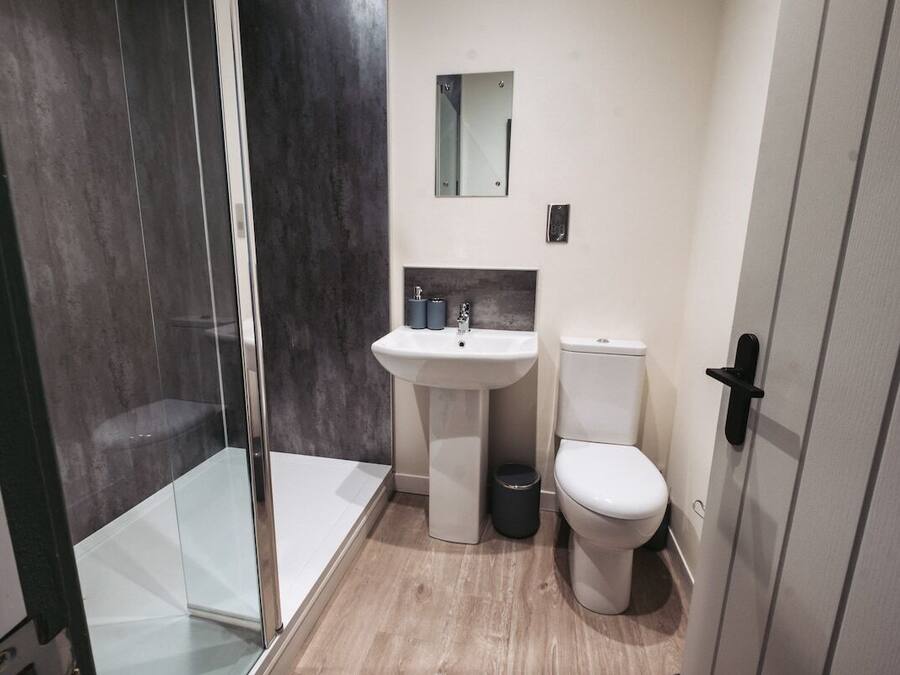 A bathroom with a glass shower enclosure, a pedestal sink, a toilet, and a mirror above the sink.