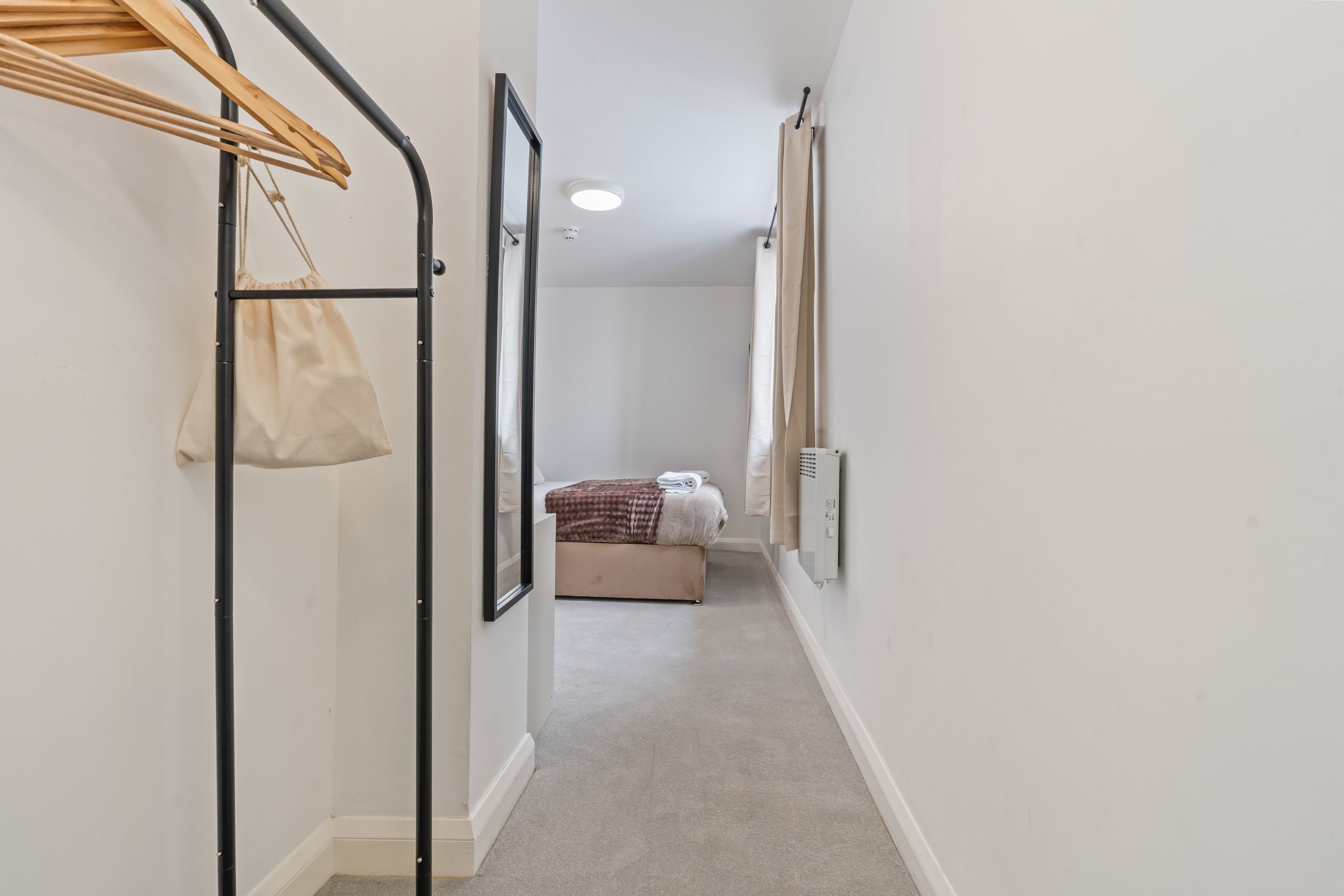 Un pasillo que conduce a un dormitorio con cama, un radiador y una bolsa colgada.