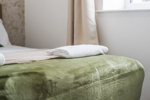 Un lit bien fait, avec une couverture verte et une serviette blanche pliée posée sur le dessus.