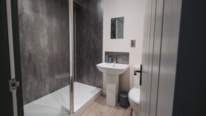 Un baño moderno con cabina de ducha de vidrio, un lavabo blanco y un inodoro.