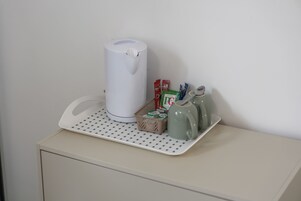 Una kitchenette con cafetera, bolsitas de té, un cartón de leche y un hervidor en una bandeja.