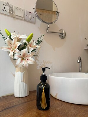 Une salle de bain avec un lavabo blanc, un miroir rond et un vase de fleurs posé sur le comptoir.