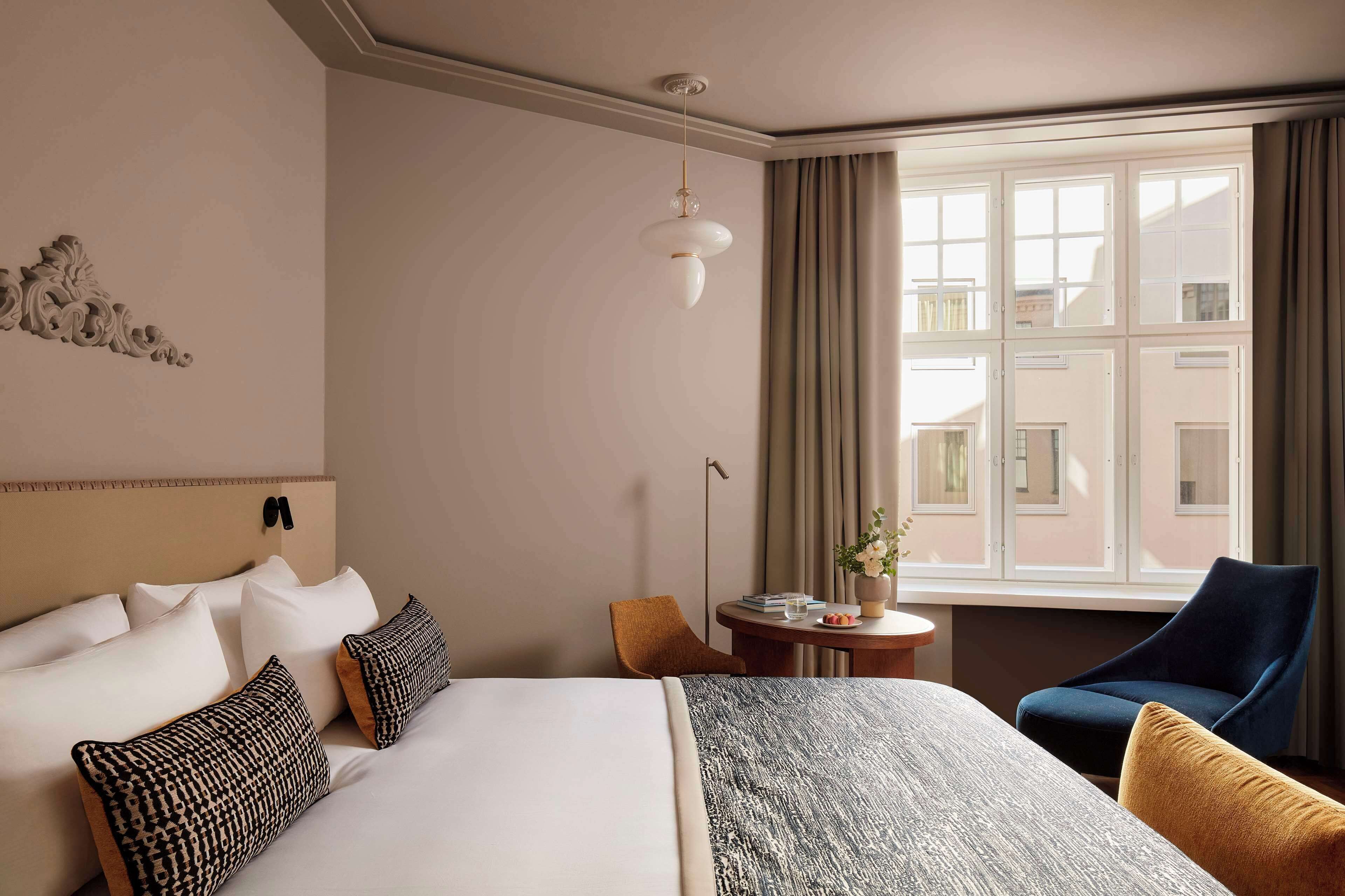 Een hotelkamer met een groot bed, een stoel, een klein tafeltje met een plant en een raam met gordijnen.
