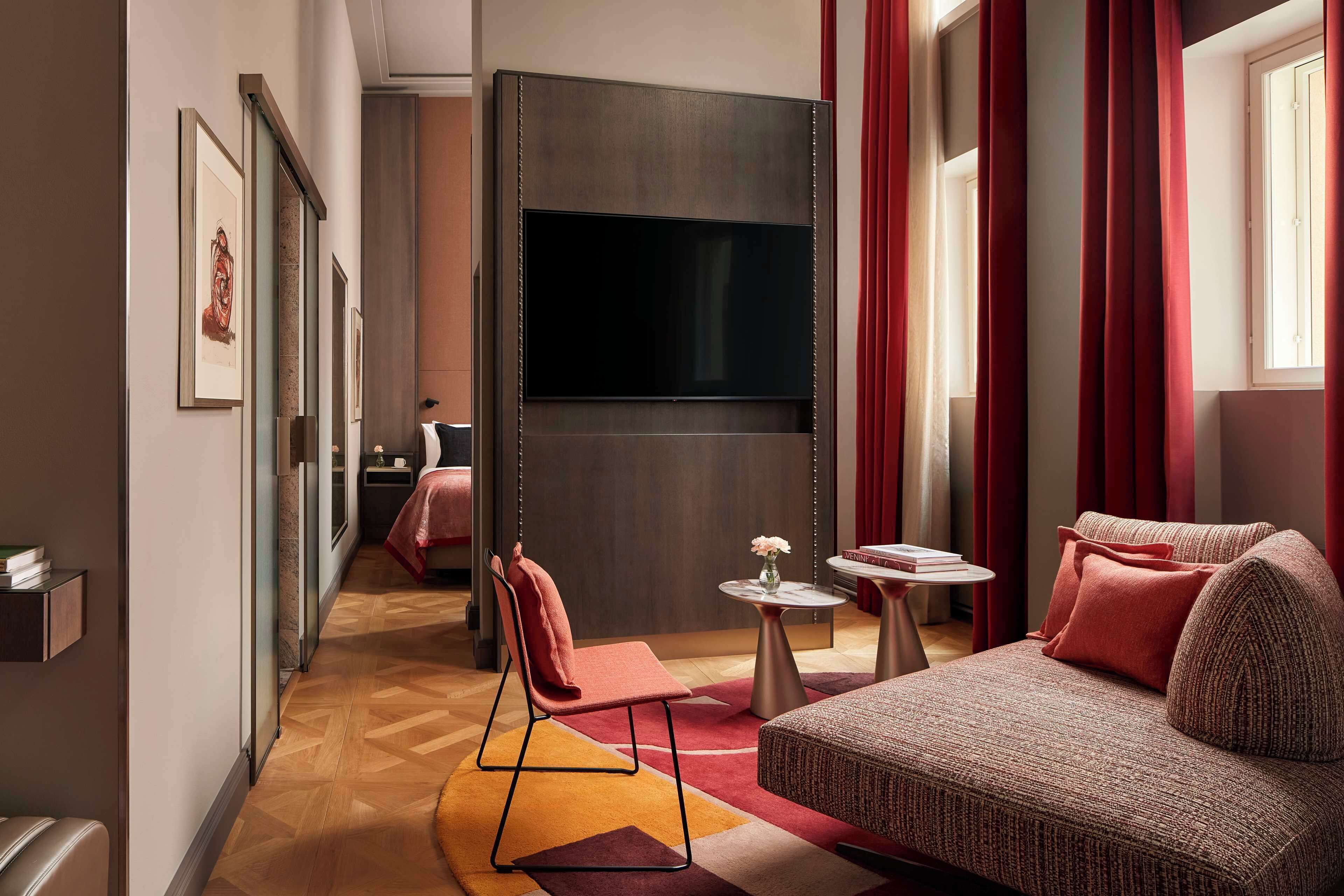 Ein modernes Hotelzimmer mit einer Couch, einem kleinen Tisch, einem Fernseher und einem Bett.
