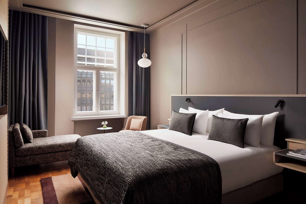 Ein modernes Hotelzimmer mit einem großen Bett, einer Couch, einem kleinen Tisch und einem Fenster mit Vorhängen.