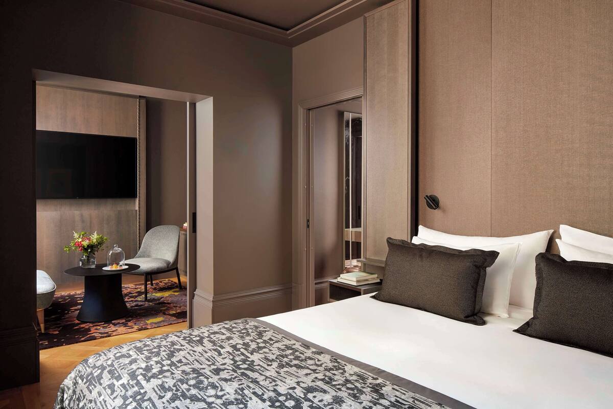 Ein Hotelzimmer mit einem großen Bett, einem Sessel, einem kleinen Tisch mit einer Vase und einem Fernseher.