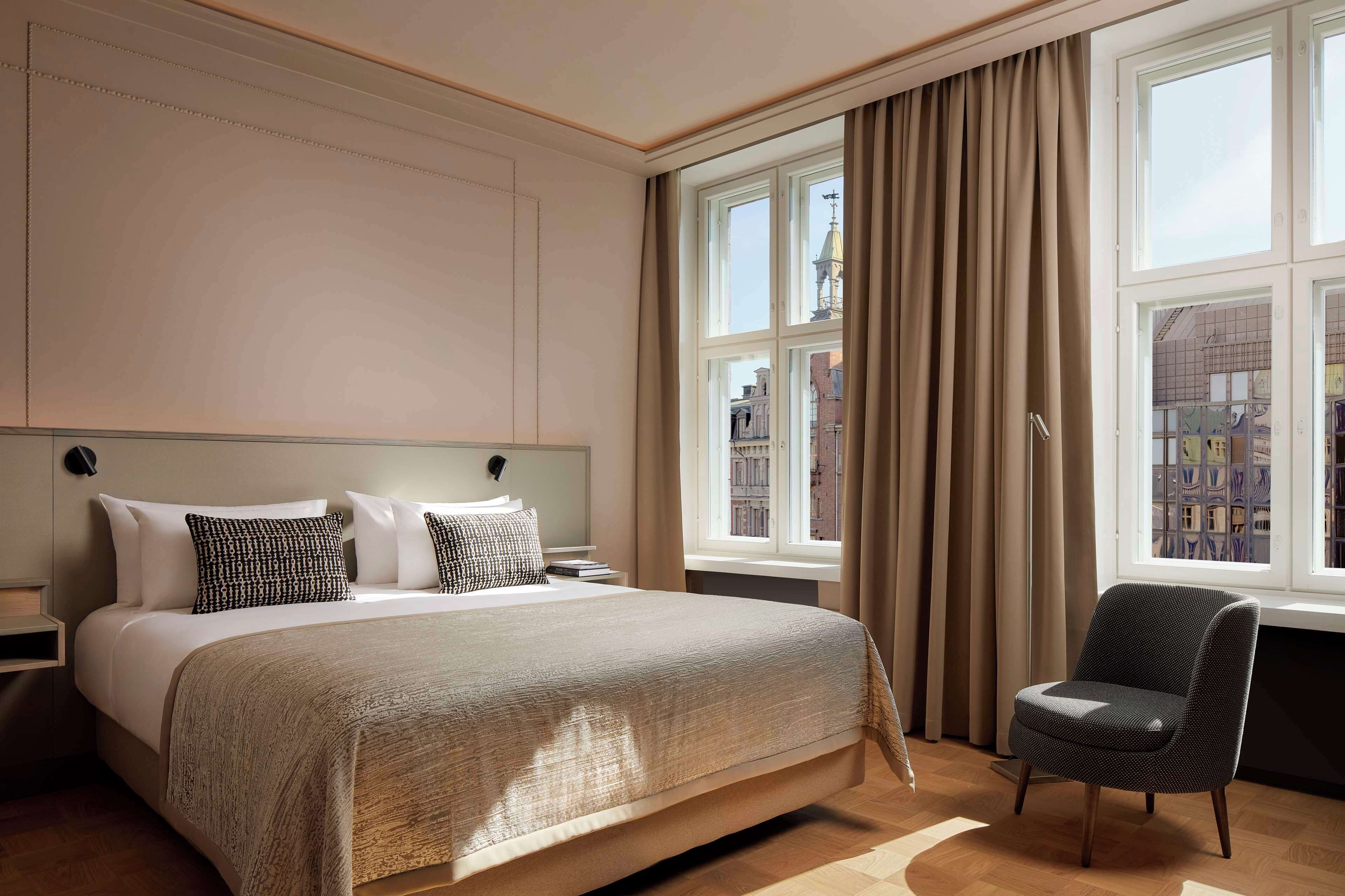 A hotel room with a large bed, a chair, and a window with curtains.