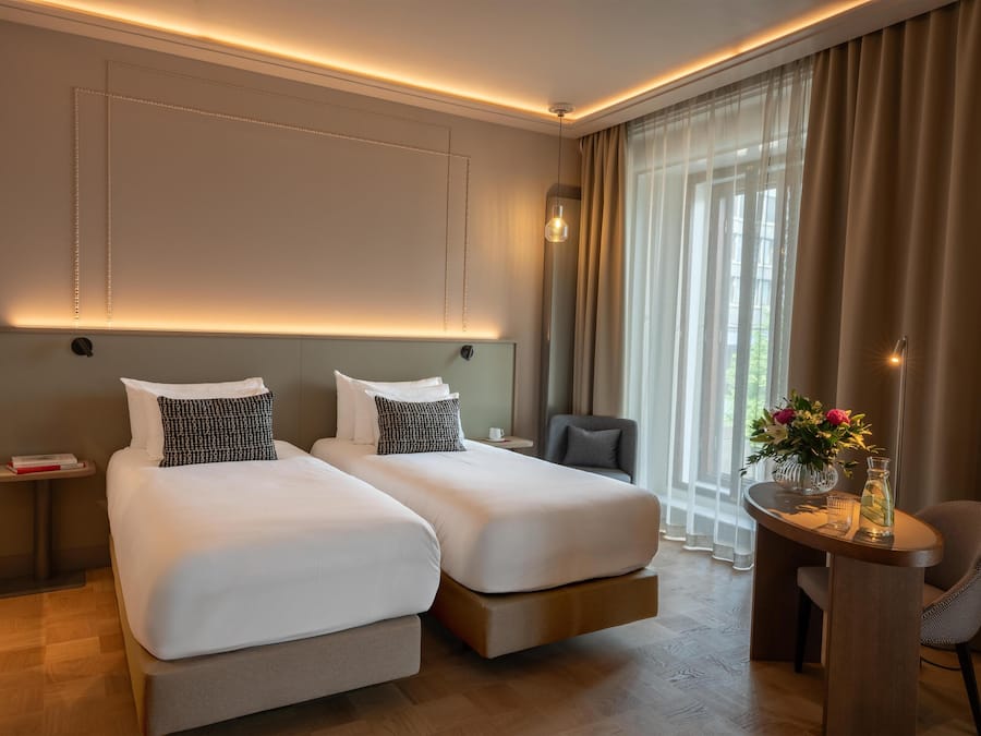 A hotel room with two beds, a small table with a vase of flowers, and a chair.