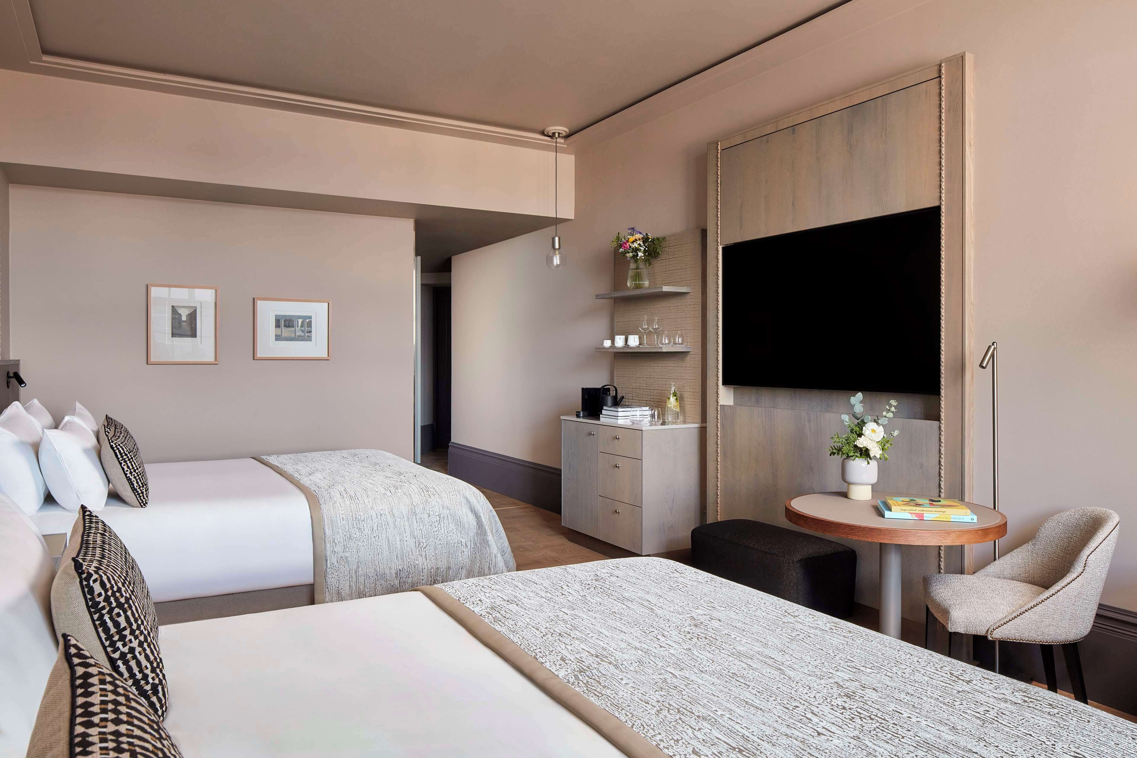 Habitación de hotel con dos camas, un escritorio, una silla, un televisor y una pequeña mesa con un jarrón de flores.