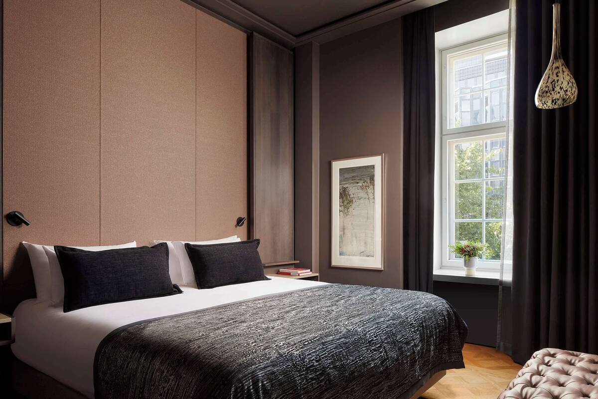 Ein modernes Hotelzimmer mit einem großen Bett, einem Nachttisch, einem gerahmten Kunstwerk und einem Fenster mit Vorhängen.