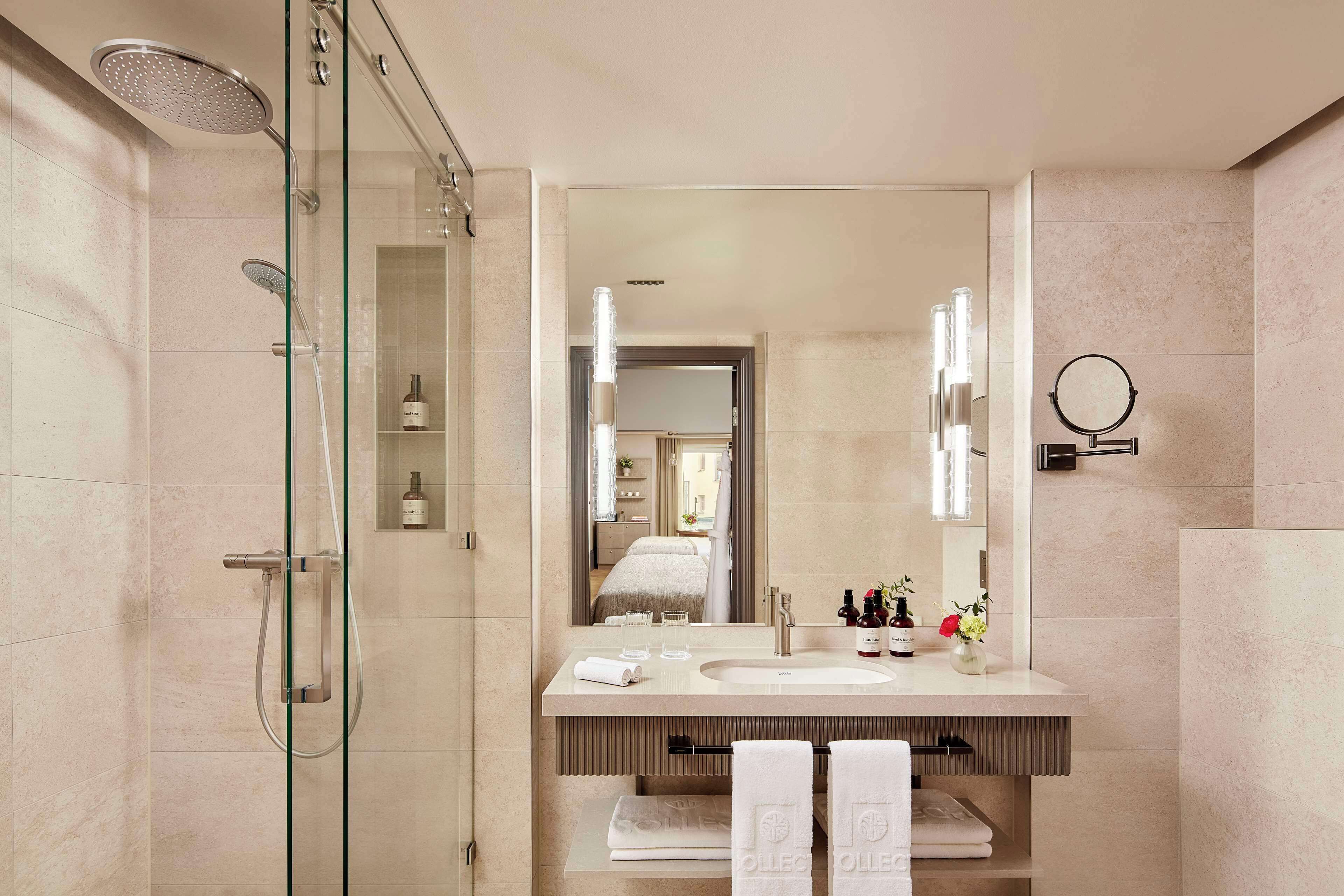 Un baño moderno con cabina de ducha de vidrio, un espejo grande y tocador con lavamanos y toallero.