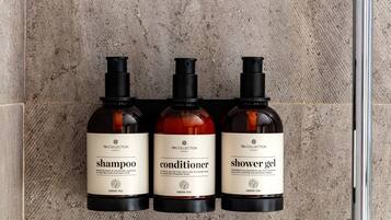 Three bottles of hotel toiletries on a textured wall.