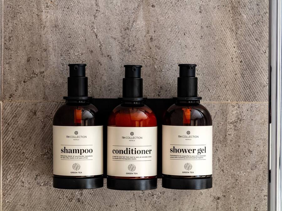 Three bottles of hotel toiletries on a textured wall.