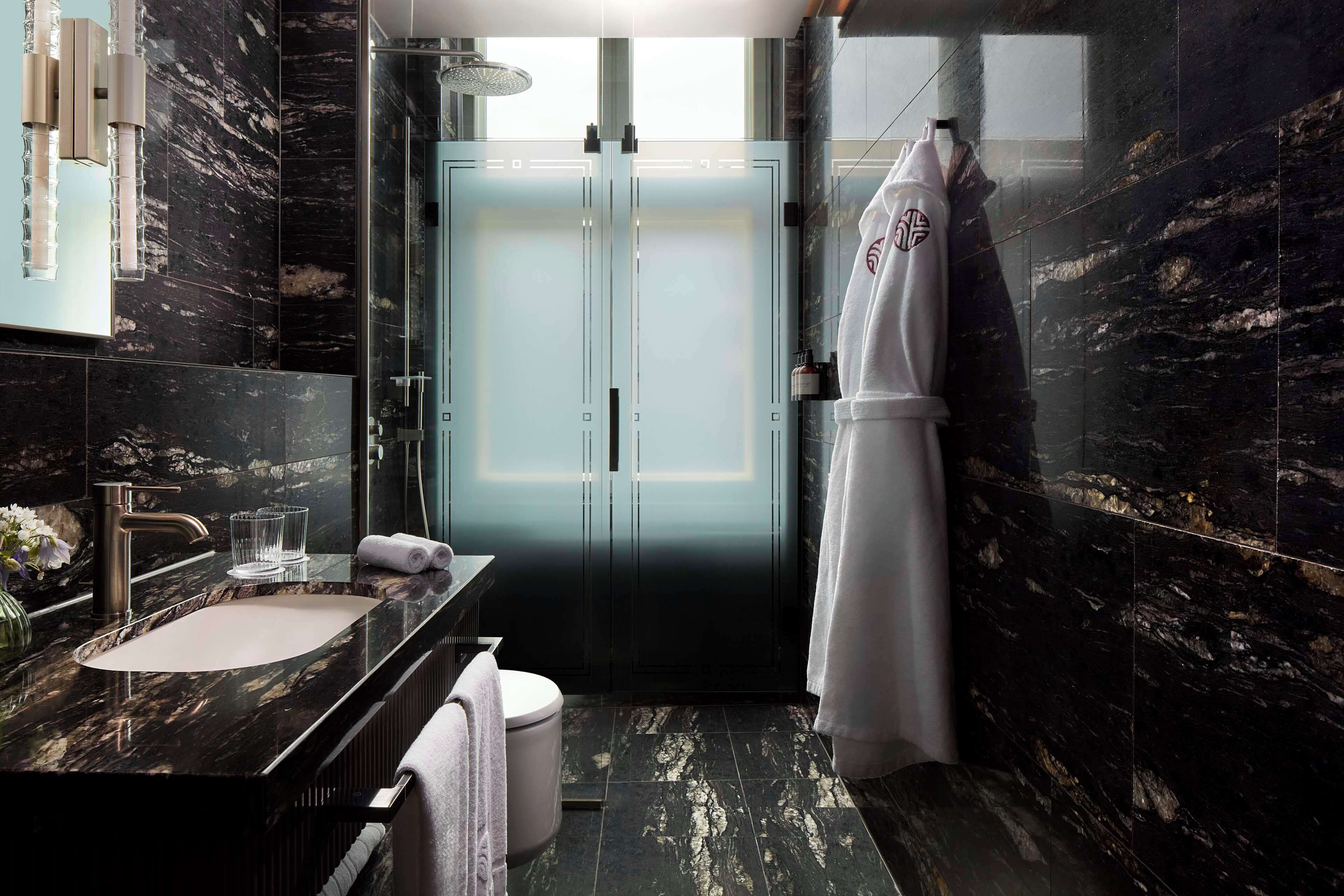 Un baño moderno con lavamanos de mármol, cabina de ducha con mampara de vidrio y un perchero para toallas.