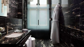 Un baño moderno con lavamanos de mármol, cabina de ducha con mampara de vidrio y un perchero para toallas.