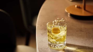 Um copo com bebida amarela e uma fatia de limão, sobre um balcão de bar.