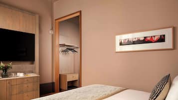 Una habitación de hotel con cama, tocador, televisión, un cuadro enmarcado y armario.