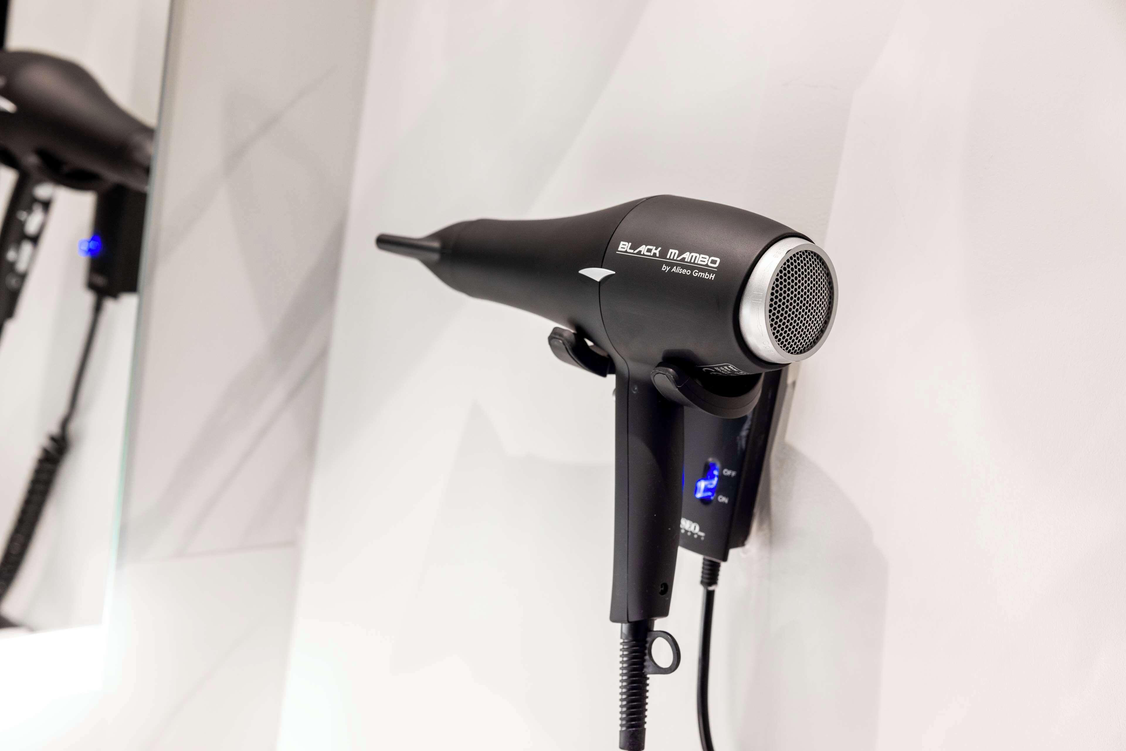 Un sèche-cheveux doté d’un écran numérique et d’un cordon d’alimentation, fixé à un mur blanc.