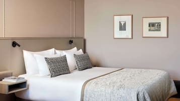 A neatly made bed with white linens and patterned pillows, a bedside table with a book, and two framed pictures on the wall.