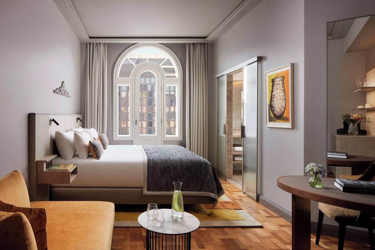 Ein modernes Hotelzimmer mit einem großen Bett, einem Essbereich und Blick durch ein Fenster.