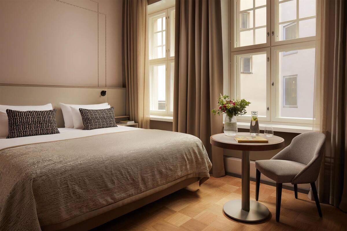 Ein Hotelzimmer mit einem großen Bett, einem runden Tisch mit Stuhl und einem Fenster mit Vorhängen.