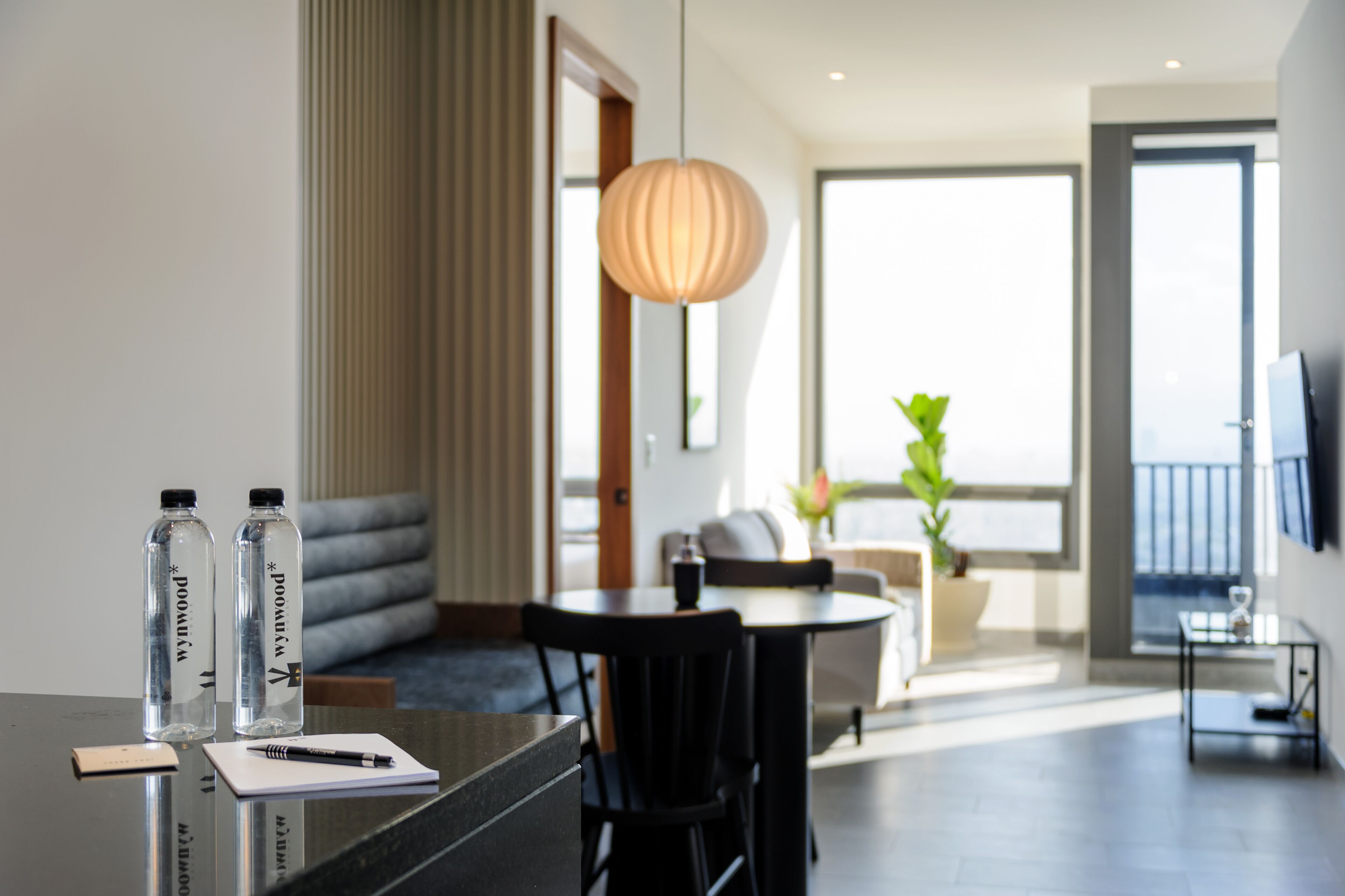 A modern hotel room with a dining area, a sofa, a table with two water bottles, a pen, and a notebook.