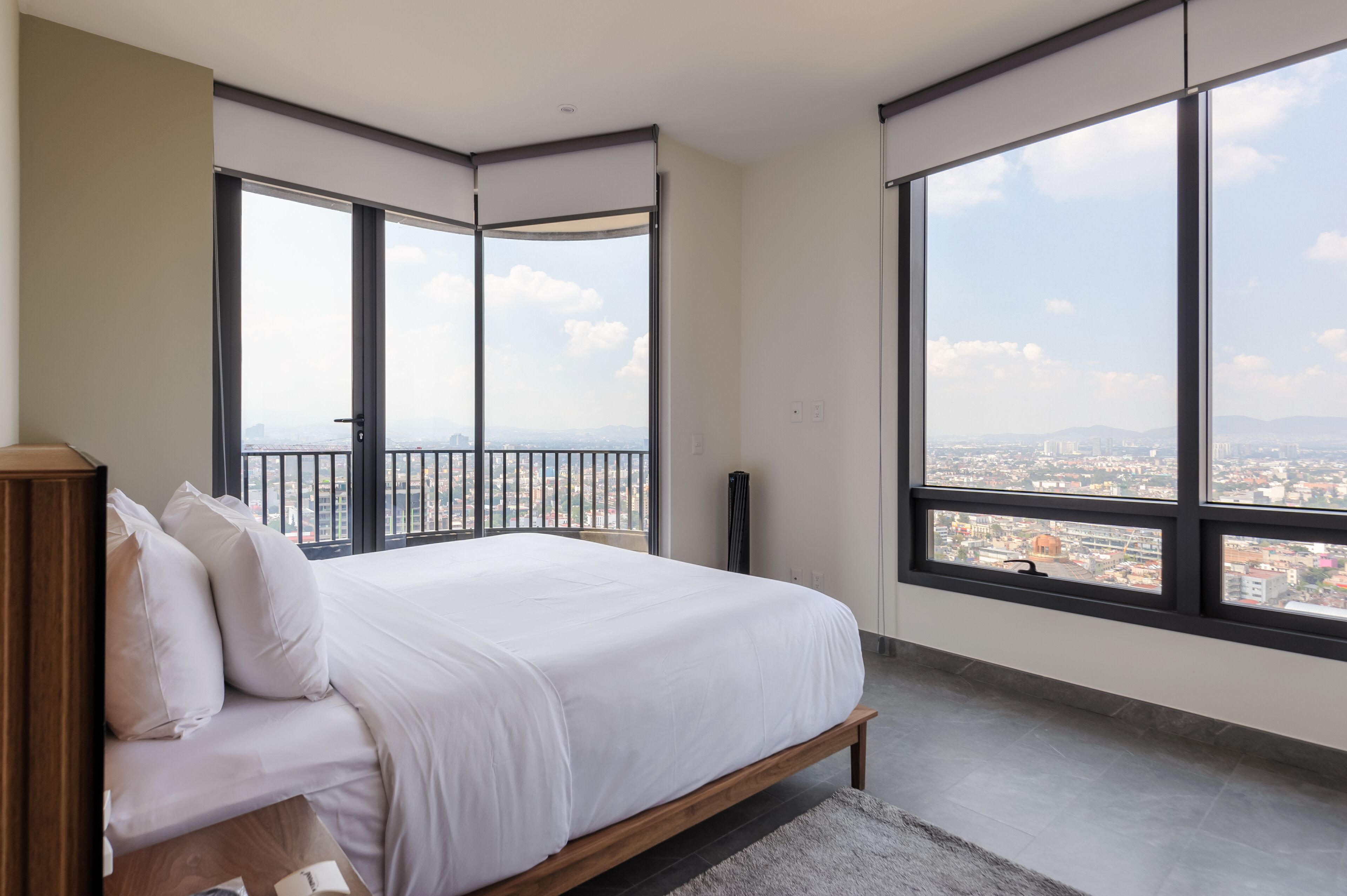 A bedroom with a large bed, a view of the city, and a balcony.