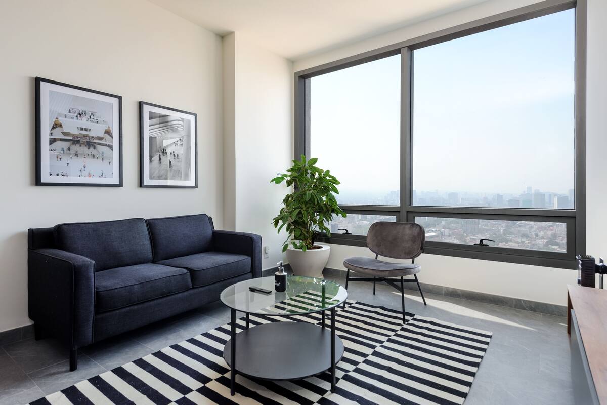 A modern living room with a large window, a sofa, a coffee table, and a potted plant.