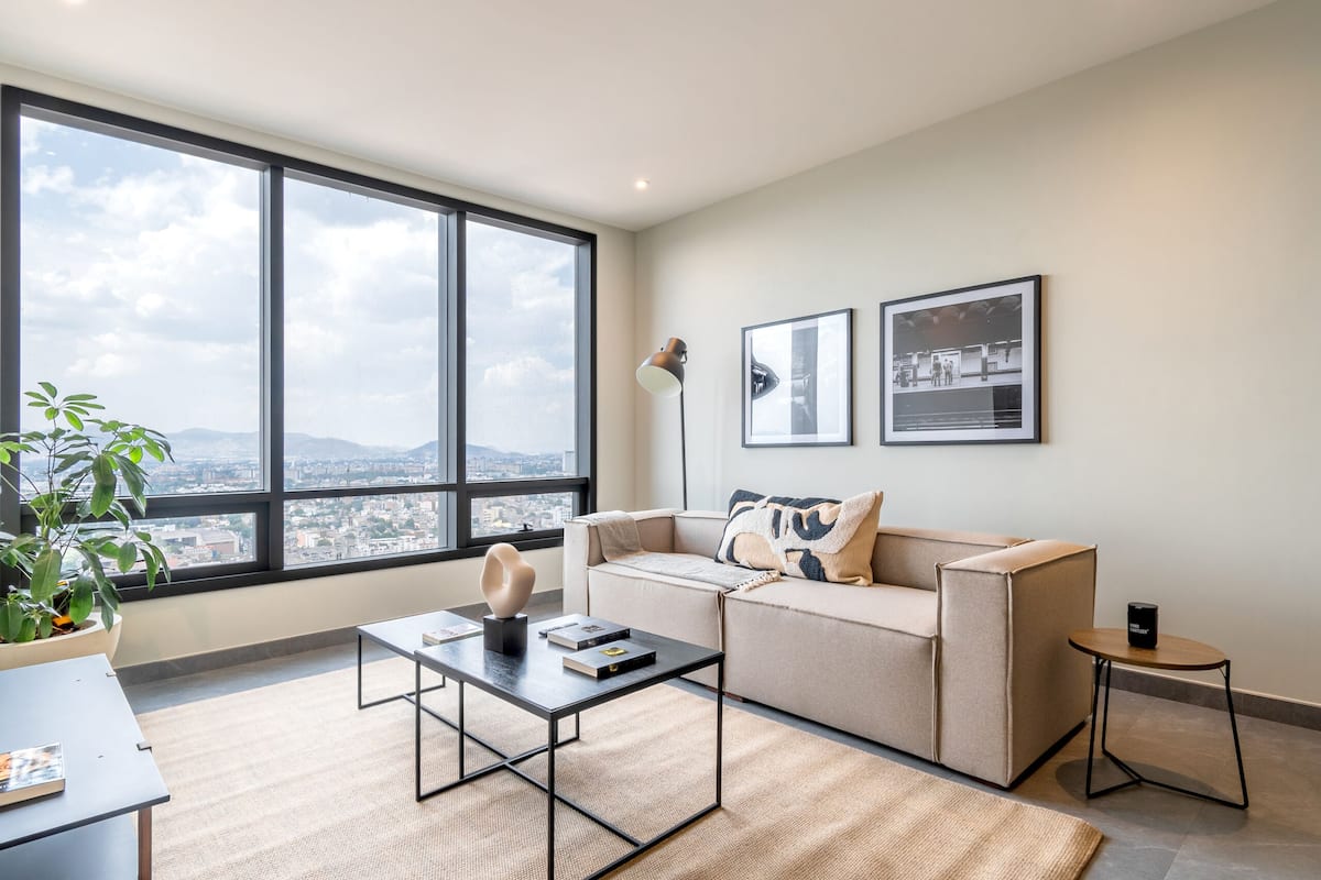A modern living room with a large window, a sofa, a coffee table, and a small side table.