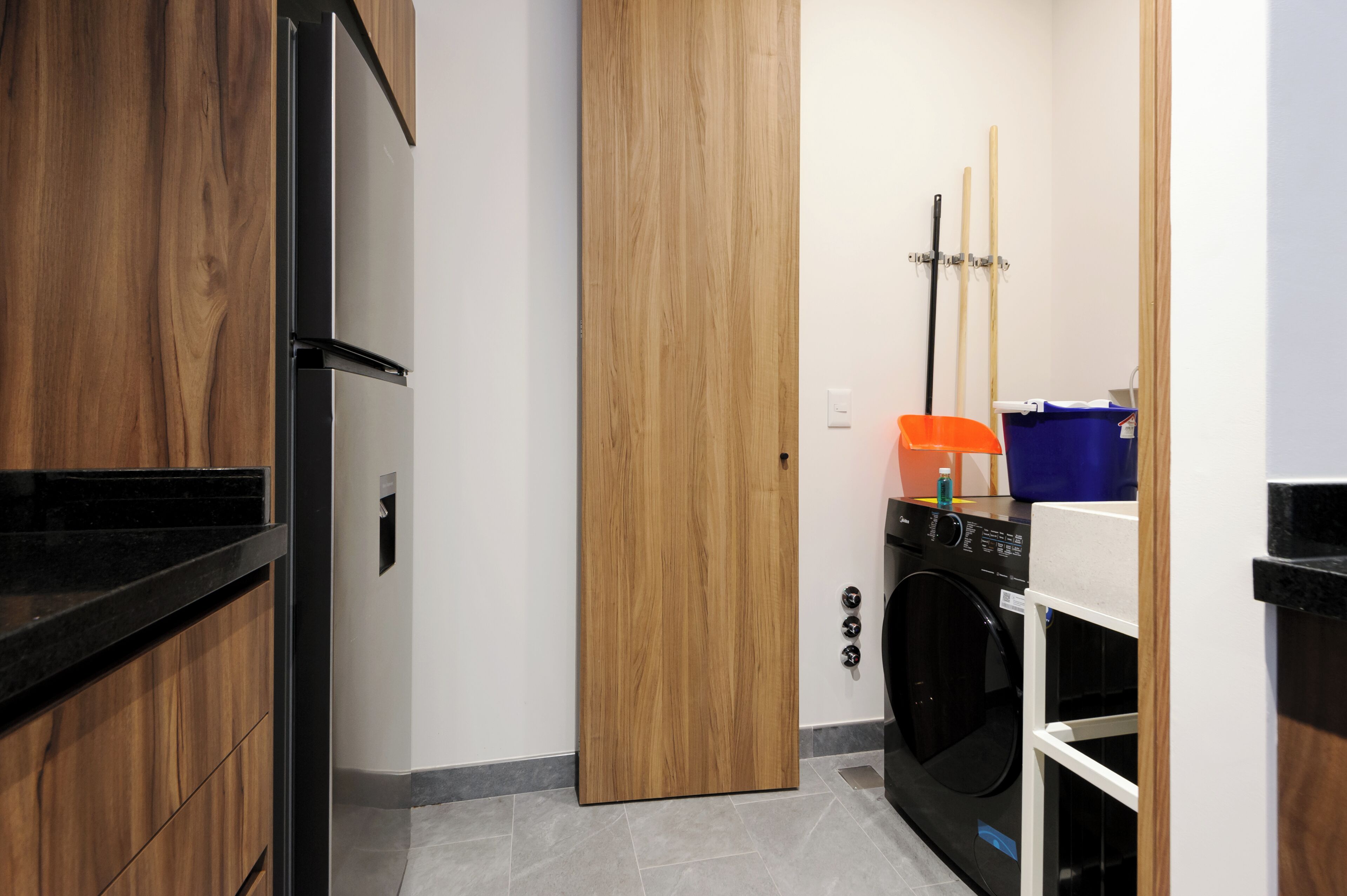 A compact laundry room with a washing machine, a drying rack, and a mop.