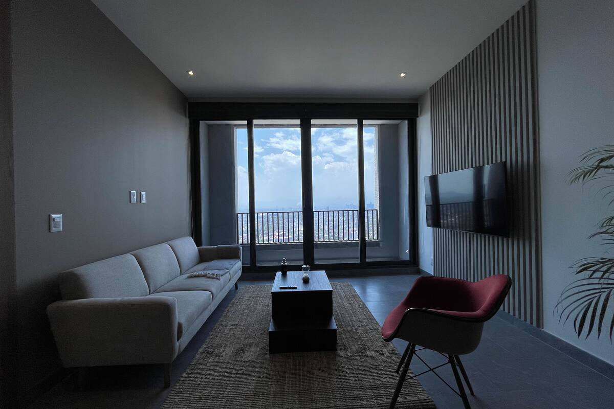 A modern living room with a sofa, a red chair, a coffee table, and a TV mounted on the wall.