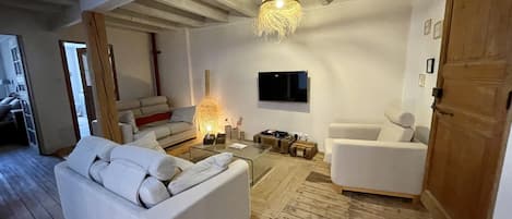 A modern living room with a sofa, armchairs, a coffee table, a TV, and a wooden ceiling.