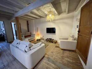A modern living room with a wooden floor, white sofas, a TV, and a hanging light fixture.