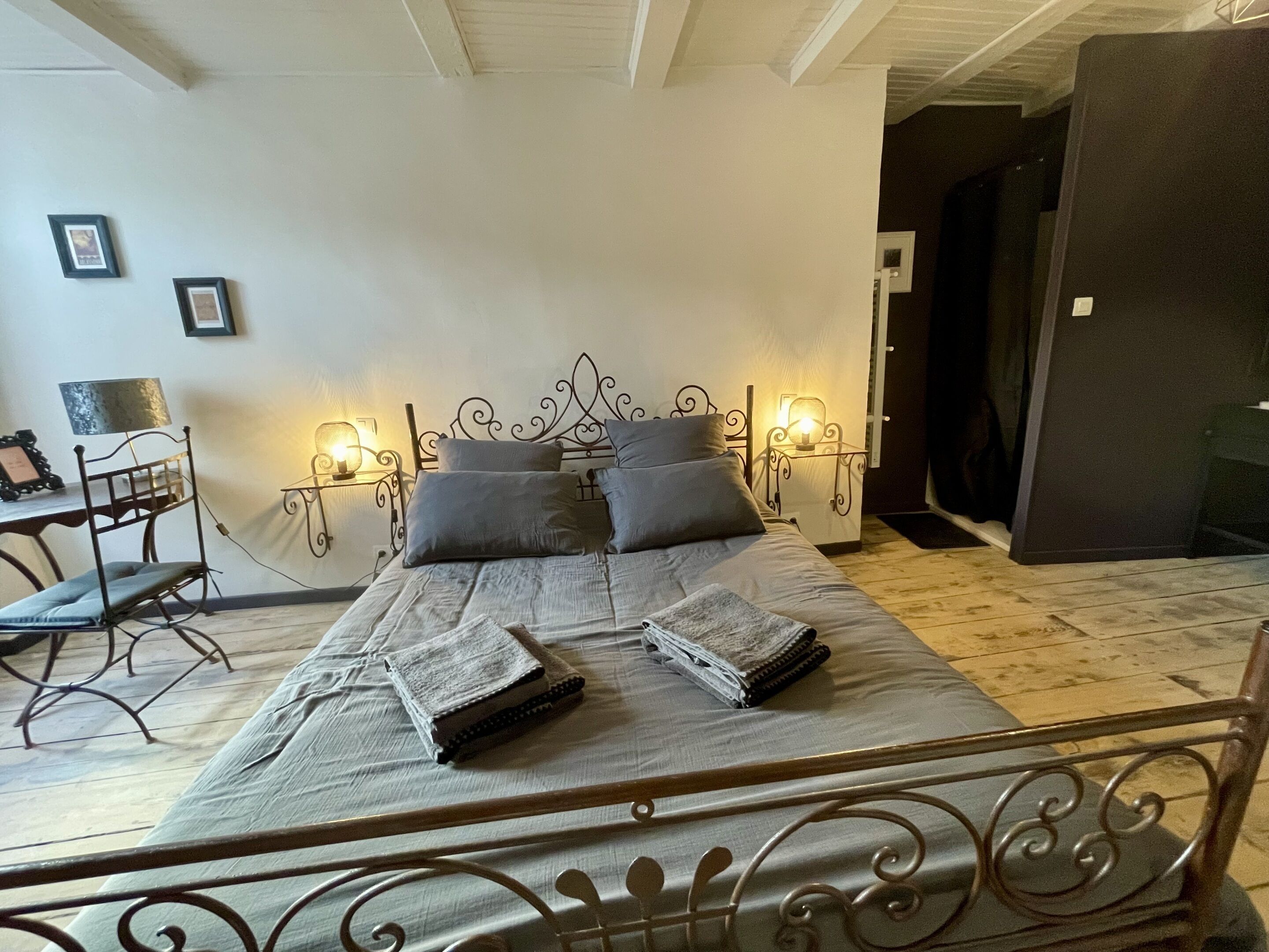 A bedroom with a metal bed frame, a bedside table with a lamp, and a chair.