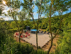 Zona de piscina con sillas rojas, un pequeño cobertizo y un jacuzzi rodeado de árboles.