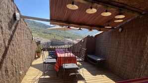 An outdoor patio with a table and chairs, a bench, and a view of the hills.