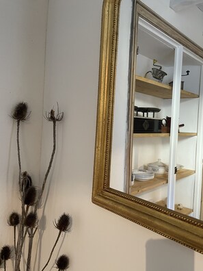 A room with a mirror, a shelf with kitchen items, and dried branches.