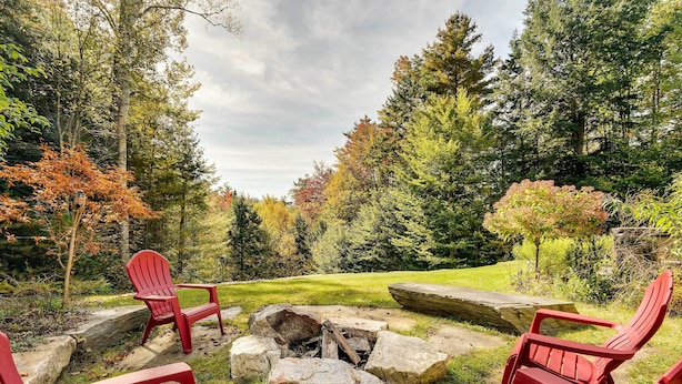 A fire pit surrounded by red Adirondack chairs in a forested area. - Winhall Home w/ Deck + Views, 6 Mi to Ski Slopes! (Winhall)