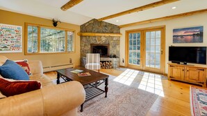 A spacious living room with a stone fireplace, large windows, a television, and a cozy seating area. - Winhall Home w/ Deck + Views, 6 Mi to Ski Slopes! (Winhall)