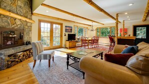 A spacious living room with a stone fireplace, wooden beams, a large window, and a cozy seating area. - Winhall Home w/ Deck + Views, 6 Mi to Ski Slopes! (Winhall)