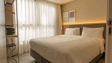 Habitación de hotel con una cama grande, un armario, un espejo y una ventana con cortinas translúcidas.