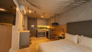 A hotel room with a bed, a desk with a chair, a small kitchenette, and a wardrobe.