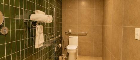 Un baño con paredes de azulejos verdes, un inodoro blanco y un pasamanos.