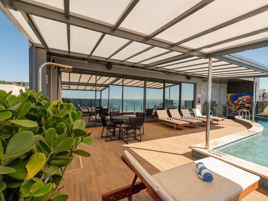 Un área de piscina en la azotea con sillones de descanso, una mesa y vista al océano.