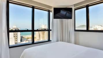 A hotel room with a bed, large windows, and a TV on the wall.
